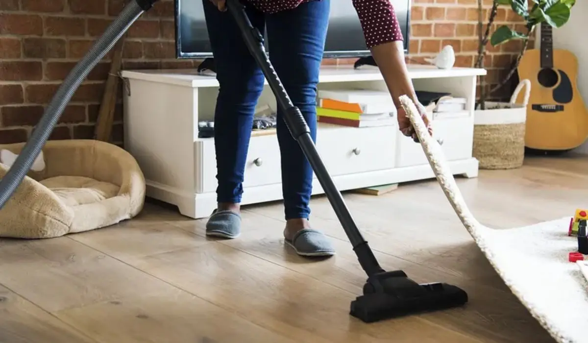a woman lifting the carpet to vacuum underneath