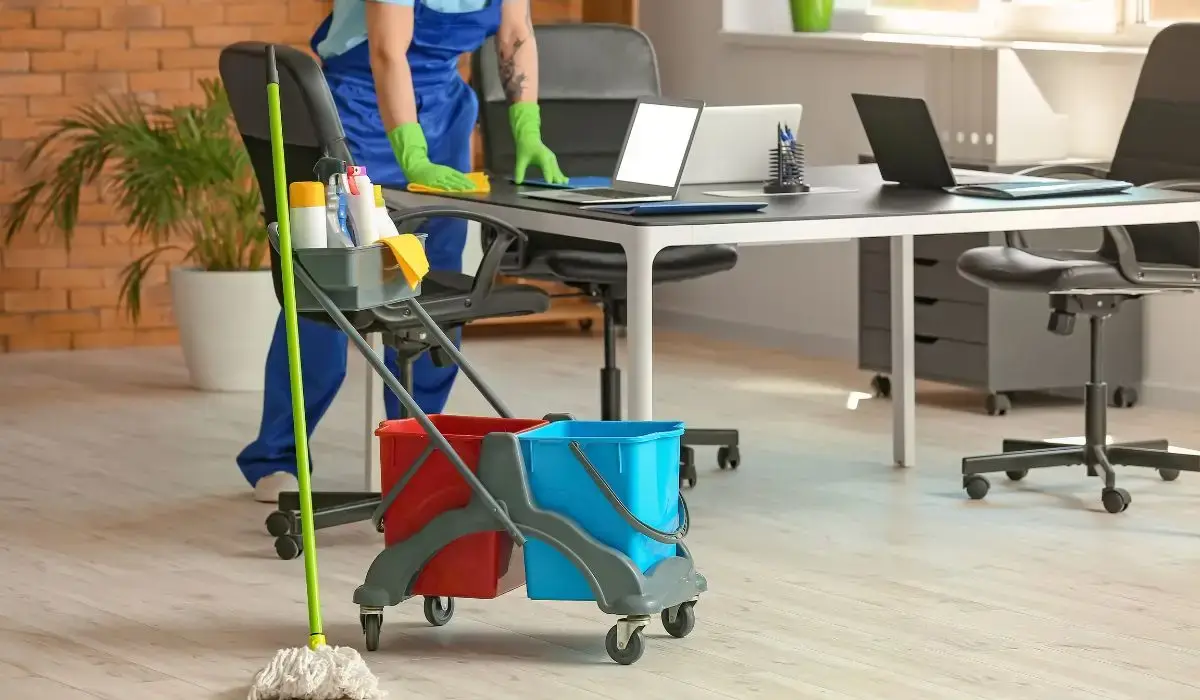 Office janitor cleaning desks with professional tools as part of a Fall Facility Checklist to prepare the workplace for seasonal health and safety needs.