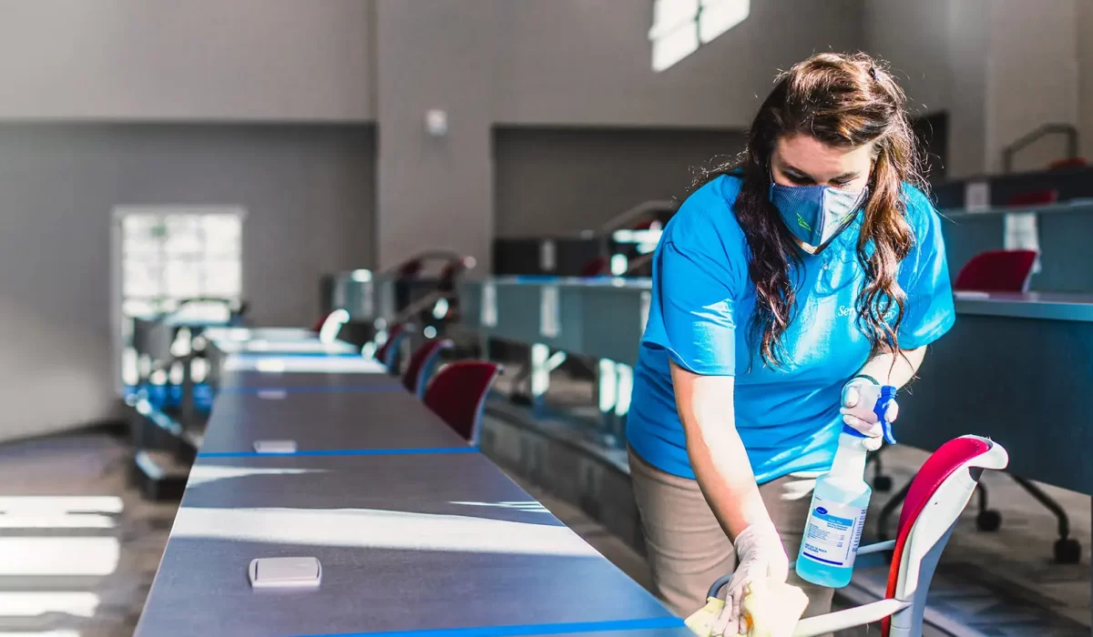 Janitorial Services vs Office Cleaning Woman disinfecting desk surface highlights the distinction in janitorial services vs. office cleaning responsibilities and focus.